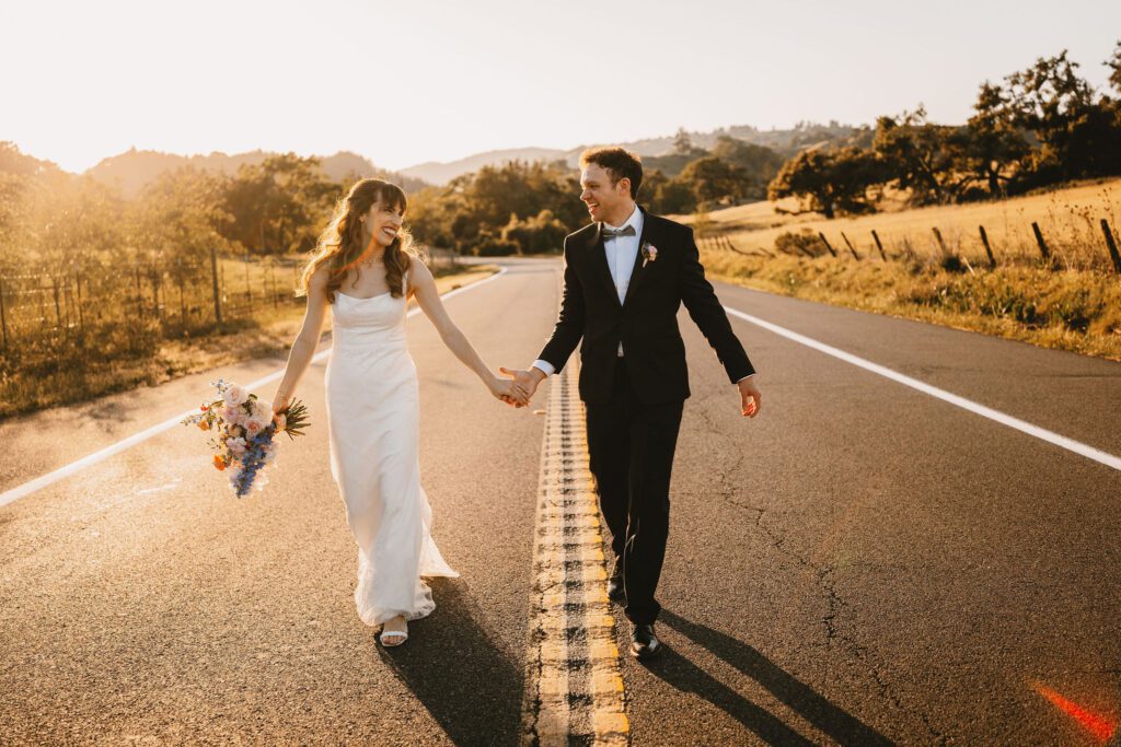 bride and groom smiling while holding hands and walking in the road at sunset at mountain house estate