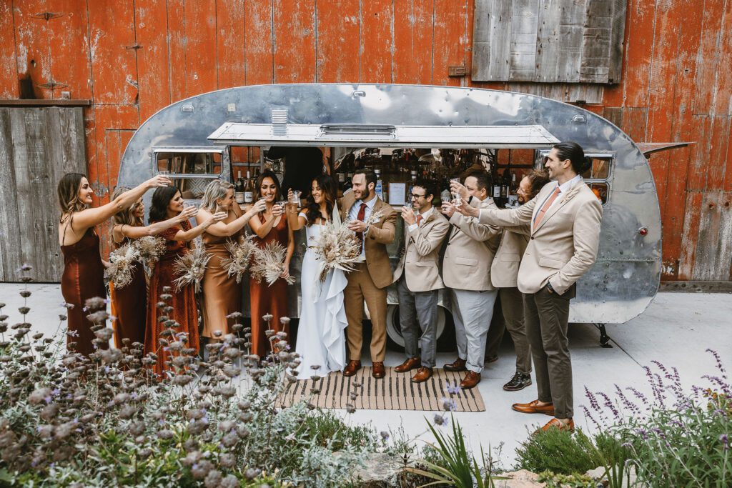 wedding party in fall colors cheersing in front of an airstream bar at stemple creek ranch