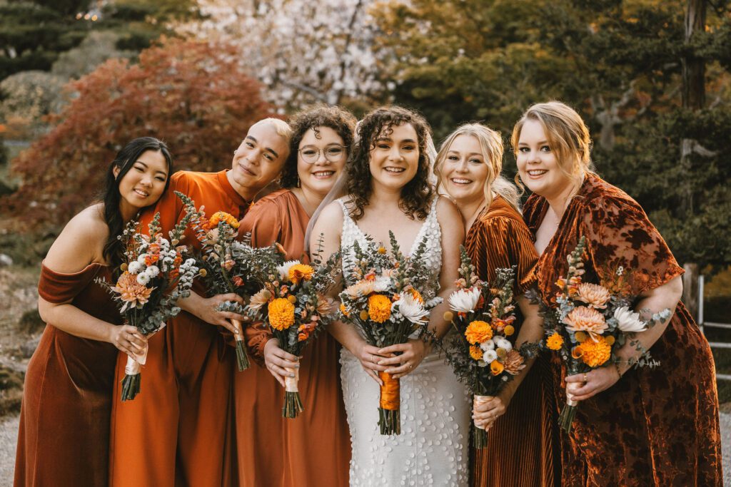 bride and bridesmaids in fall colored dresses hugging at hakone gardens in san jose california