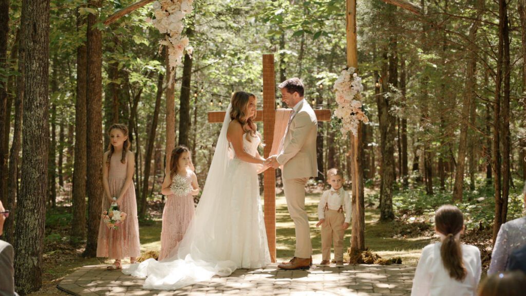 Bride and groom holding hands during their Wedding in the Woods ceremony with their children at their feet at Carolina Country Weddings